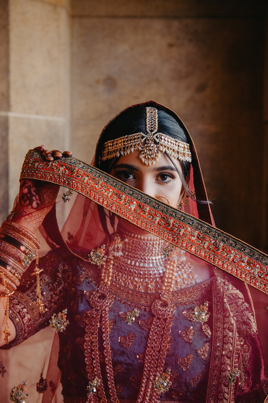 Omari photographed in maroon and gold, an embroidered veil drawn across her face